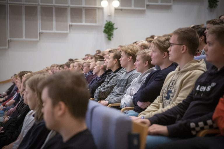 Nuoria miehiä istumassa auditoriossa.